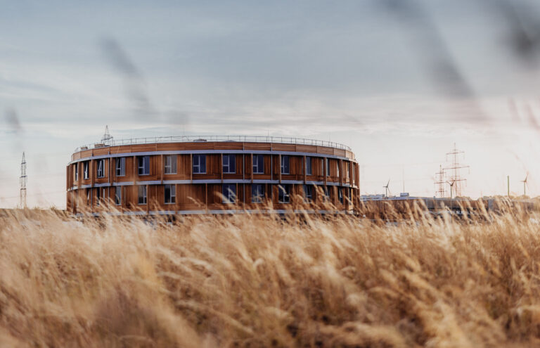 SAN Group headquarters building in a natural field landscape with modern wooden architecture.